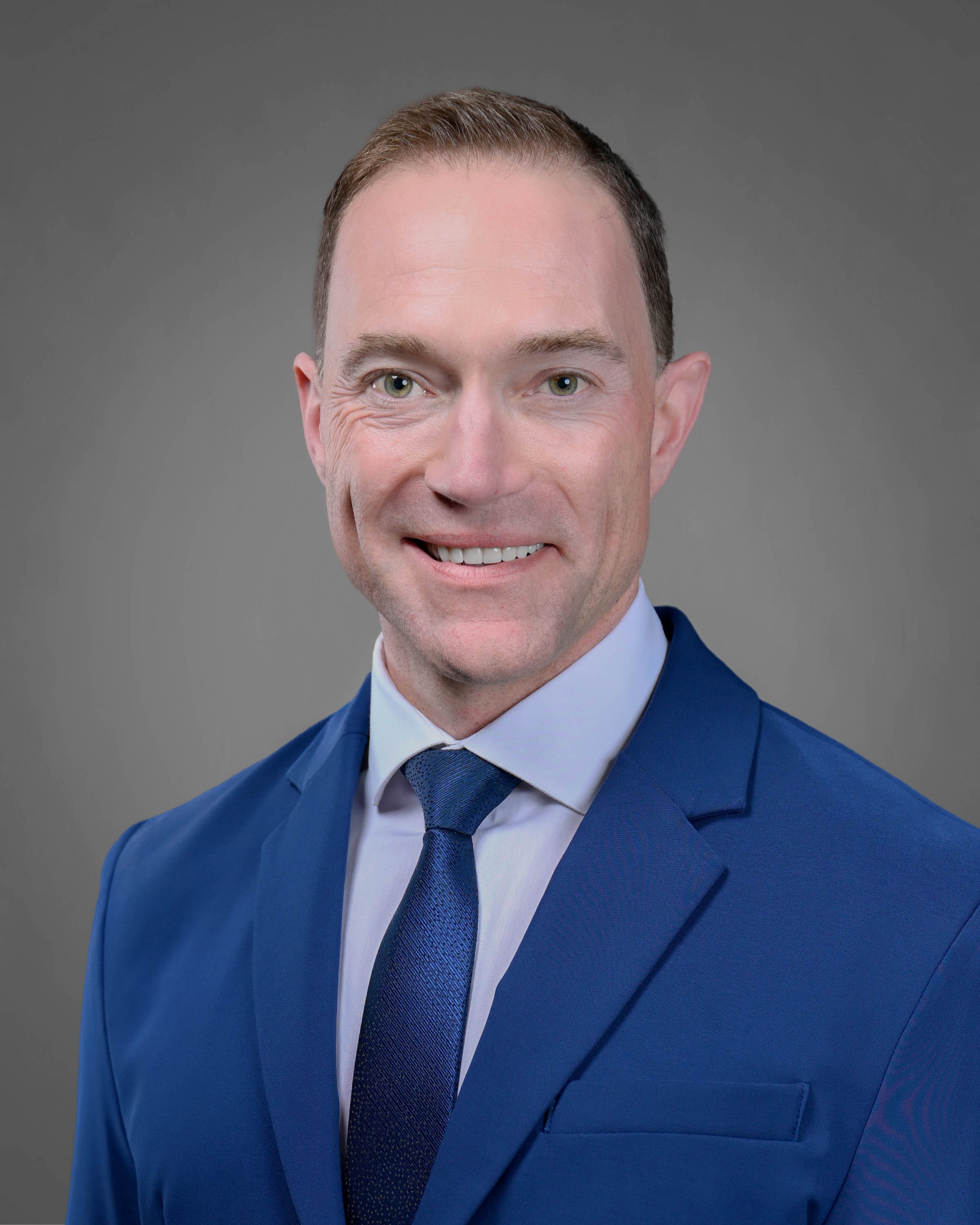 Man smiling in a blue suit with blue tie